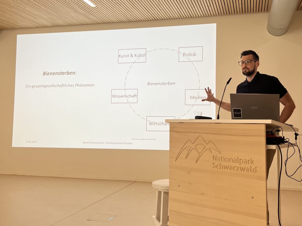 Daniel Bräunling am Rednerpult, im Hintergrund eine Präsentation zum Thema Bienensterben.